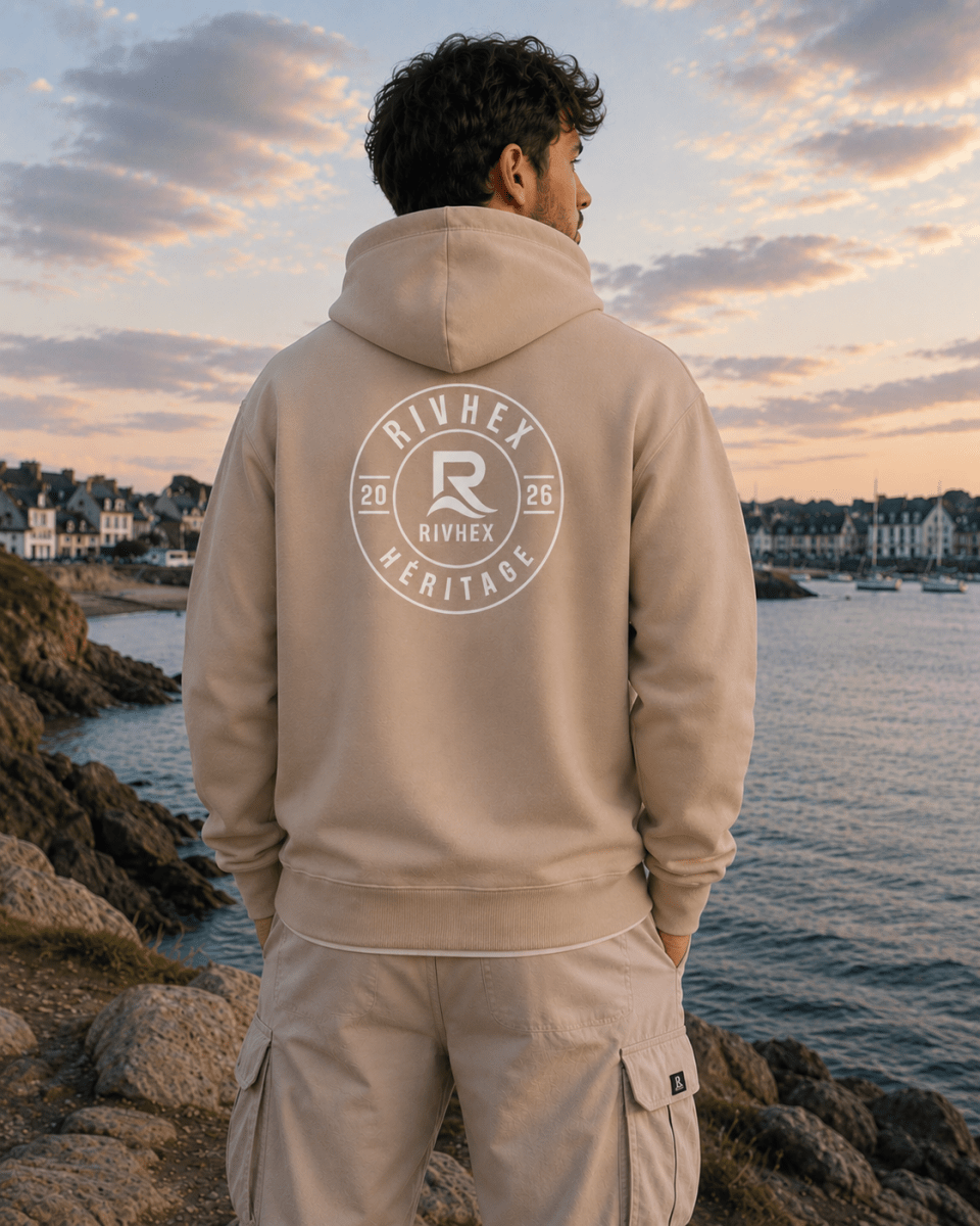 Sweat à capuche Héritage RIVHEX beige porté de dos en bord de mer, emblème circulaire blanc