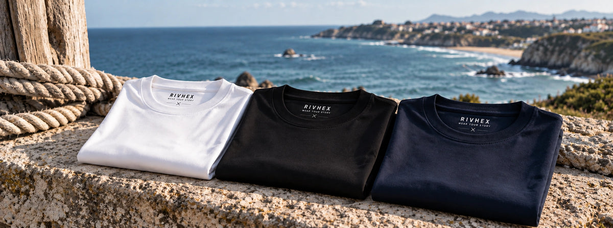 3 ACCESS T-shirts in white, black and navy blue laid on a low wall by the sea